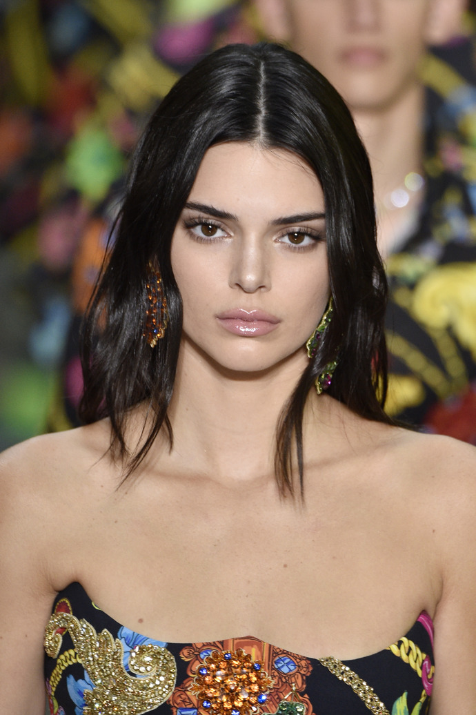 Skvělý tip na zvětšení očí jsou stíny pod dolním víčkem. Ty Jenner předvedla na přehlídce Versace SS19. Romatický look je doplňený narůžovělým leskem na rty a perfektně naneseným highlighterem. 
