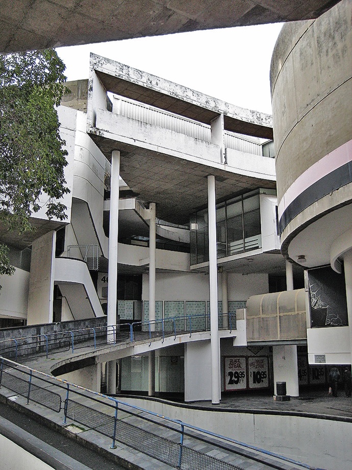  

Werdmuller Centre, 1975

Dnes uzavřené obchodní středisko Werdmuller stále vyvolává rozporuplné emoce a poslední roky čelí hrozbám demolice. Té se odborná veřejnost snaží zabránit a poukazuje na nesporné kvality stavby. Architekt Roelof Uytenbogaardt v ní experimentoval s otevřeným prostorem, rampami ze surového betonu a dramatickými světelnými průhledy. Struktura měla navodit dojem otevřeného tržiště pro zákazníky všech kultur, do myšlenky ale zasáhlo prohlášení čtvrti za striktně bělošskou a nucené vystěhování zbytku obyvatelstva.
