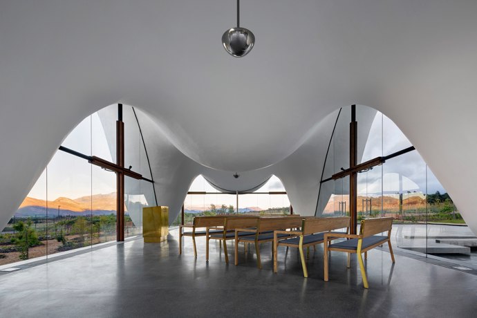  

Kaple BOSJES, 2017

Objekt na vinici nedaleko Kapského Města vzešel ze spolupráce britského Steyn Studia a jihoafrických TV3 Architects. Divoce rozvlněná baldachýnová střecha se vznáší nad prosklenými stěnami a tvarově vzdává hold historickým holandským štítům, typickým pro oblast Západního Kapska. Interiér je úsporný – jednoduché dřevěné lavice a zlatavý pulpit svou prostotou navádějí návštěvníkovo oko zpátky ven, k sadu s granátovými jablky a okolním horám. 
