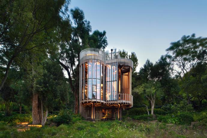  

Malan Vorster Treehouse, 2017

Ztracen v okolo rostoucí zeleni, Treehouse od jihoafrického studia Malan Vorster připomíná tajnou dětskou skrýš v koruně stromu. Přání investora, který měl na pozemku již rodinnou vilu, bylo získat samostatný a zcela oddělený prostor – útočiště, kde by mohl být zcela o samotě. Architekti zadání vyřešili formou čtyř vzájemně propojených válcových věží, vynesených na pilotech. Dřevěné lišty na fasádě propouštějí světlo, ale zároveň zajišťují potřebné soukromí. 
