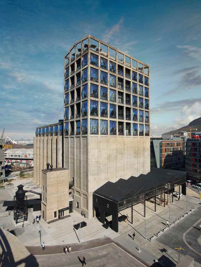  

Zeitz MOCAA, 2017

Kdysi nejvyšší budova subsaharské Afriky, silo v přístavu Kapského Města, dnes slouží jako muzeum současného afrického umění. Britský architekt Thomas Heatherwick proměnil dvaačtyřicet vysokých tubusů na uchování kukuřice na impozantní atrium s téměř katedrální atmosférou. Kolem atria umístil v několika patrech různě velké výstavní galerie a na střechu sochařskou zahradu. V exteriéru zaujmou rozměrná okna, jež svým vypouklým tvarováním naznačují obrovský tlak, jemuž bylo silo kdysi vystaveno. 
