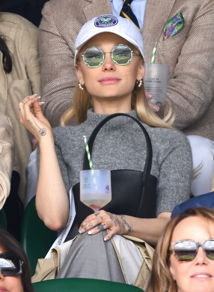  

Zpěvačka Ariana Grande byla spatřena na tribunách v šedém pleteném topu a sukni Ralph Lauren, se slunečními brýlemi Tiffany & Co s kulatými obroučkami a wimbledonskou kšiltovkou.
