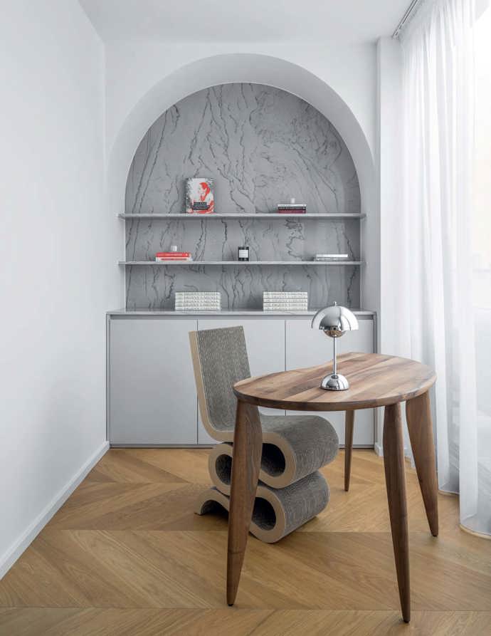 Výklenek je obložený stejným kvarzitem Quarzite White Silk jako kuchyně, aby spolu oba prostory komunikovaly. Na stolku od FermLiving svítí chromová lampička Flowerpot od &tradition a její obliny si krásně rozumějí se záhyby křesla Wiggle od Franka Gehryho pro Vitru.