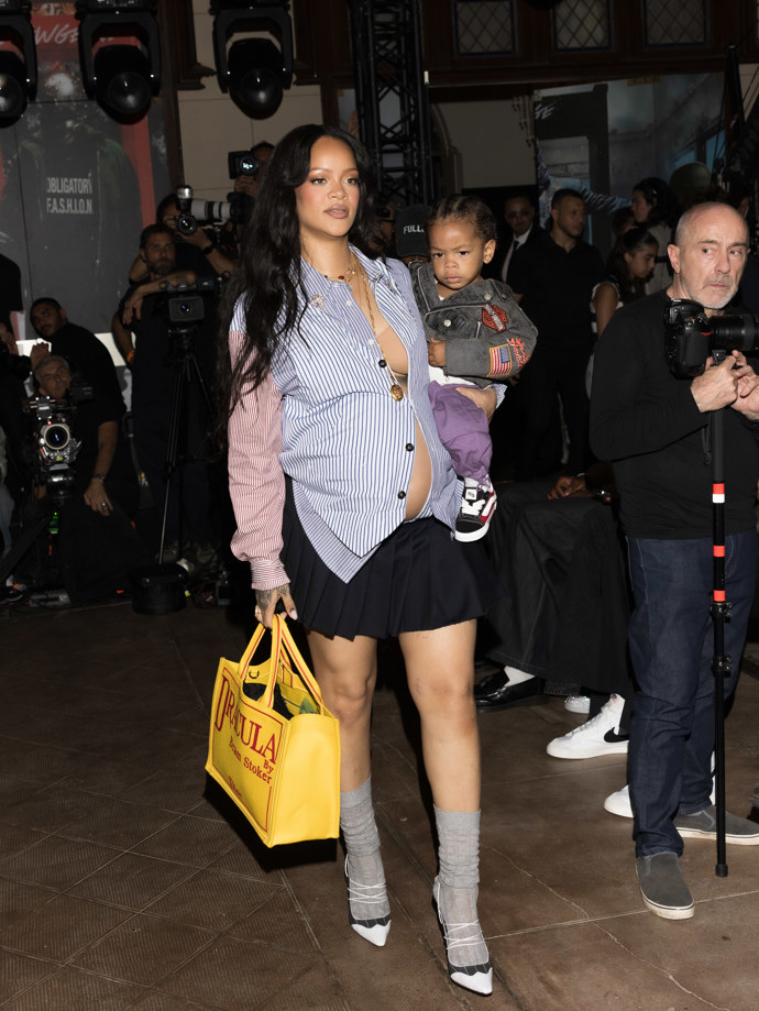  Na pařížském Men’s Fashion Weeku dorazila Rihanna podpořit módní značku svého partnera A$AP Rockyho. Na ruce nesla jejich druhého syna Riota, a přitom stihla předvést look, který okamžitě obletěl módní rubriky: polorozepnutou pruhovanou košili, námořnickou mini sukni a šedé ponožky sladěné s páskovými podpatky.