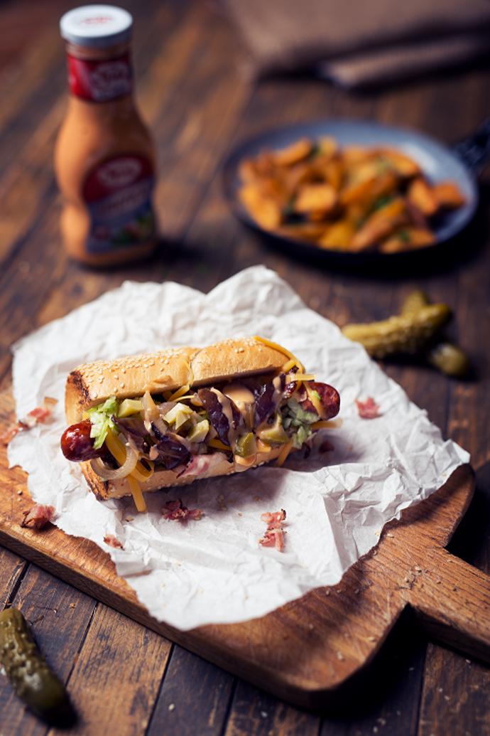 Americký hot dog

Suroviny:

4 nožičky kvalitních hovězích párků 
4 brioškové bagetky 
1/2 ledového salátu 
10 dkg čedaru 
10 dkg anglické slaniny 
1 červenou cibuli 
2 nakládané okurky 
100 ml Amerického dressingu Spak 

Postup: 

Cibuli a okurky nakrájíme nadrobno a smícháme s Americkým dressingem Spak. Slaninu si nakrájíme na tenčí proužky a opečeme dokřupava. Čedar si nastrouháme na hrubším struhadle. Ledový salát nasekáme nadrobno. Bagetky si v půlce nakrojíme a opečeme ze všech stran, poté do nich vložíme párky, které zasypeme nastrouhaným čedarem, opečenou slaninou, ledovým salátem, a nakonec přidáme Americký dressing Spak.