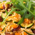 Dýňové rizoto:
Postup:
1 kg dýně Hokkaido
300 g rýže Arborio (kulatozrnná rýže)
1 l zeleninového vývaru
200 ml bílého vína
1 cibule
máslo
sůl a pepř
parmazán
petrželka.
Postup:
Vydlabanou neoloupanou dýni Hokkaido nakrájíme na menší kostky, cibuli nadrobno. Na másle osmahneme cibuli, poté přidáme dýni a osmažíme ze všech stran. Přisypeme (nepropláchnutou) rýži, krátce zamícháme, aby se zrníčka obalila máslem, přidáme víno. Za stálého míchání necháme část vína odpařit a přidáme asi 1 dl horkého vývaru. Ten vždy necháme vyvařit a přidáváme po decilitrech, dokud nám nedojde (dokud není rýže al dente). To by mělo trvat přibližně 25 minut. Nakonec vmícháme do rizota nadrobno nasekanou čerstvou petrželku a asi ½ lžíce másla, dochutíme solí a pepřem a podáváme posypané nastrouhaným parmazánem.