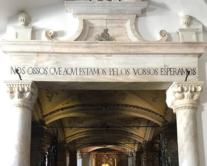 Morbidní nápis na portálu kaple v překladu znamená: My kosti zde přítomné, čekáme na ty Vaše.