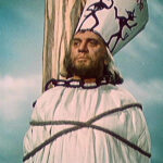 Na coroze (papírové čepici) Jana Husa je napsáno "Ecce Heresiarcha", což znamená "Pohleďte, arcikacíř".