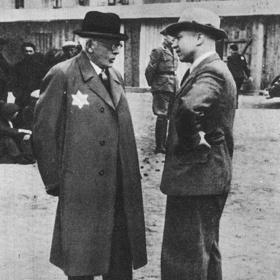 Výrobky byly určeny pro Němce, kteří nechávali lodžské ghetto fungovat déle než jiné. Na této fotce je Mordechaj Chaim Rumkowski v hovoru se svým německým nadřízeným Hansem Biebowem.