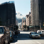 Vpředu zdánlivě klidná ulice, na pozadí lze vidět valící se oblaka popela a prachu ze Světového obchodního centra.