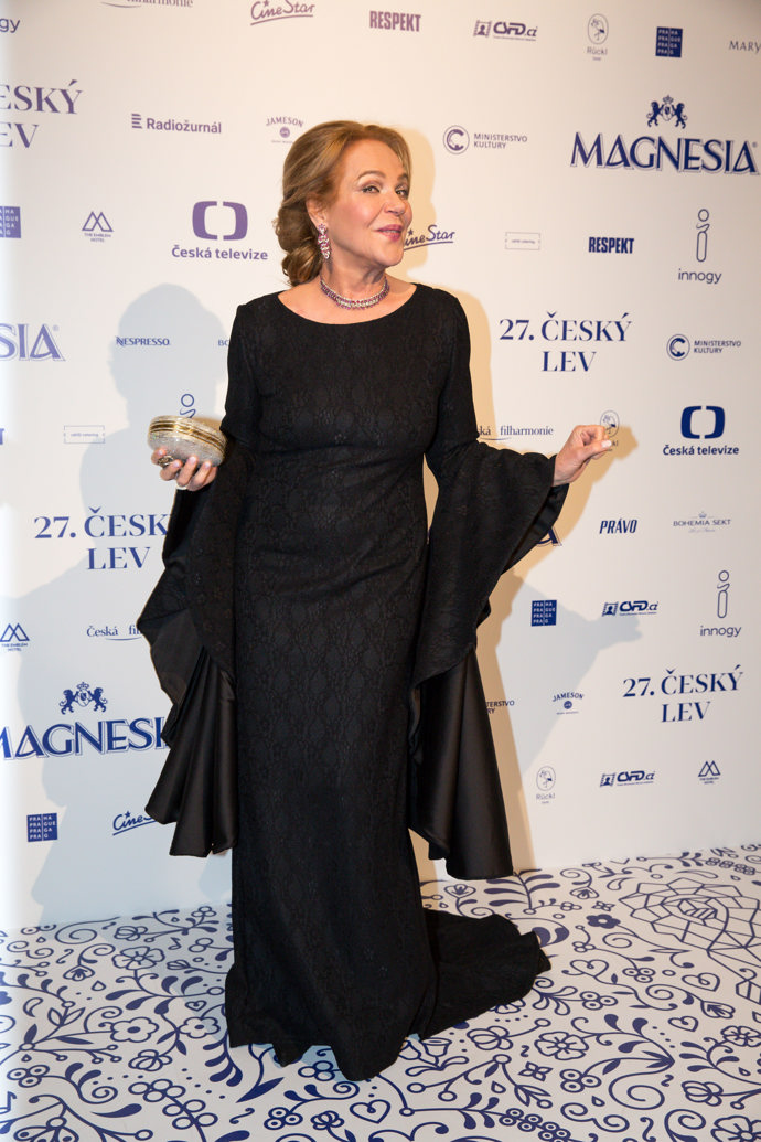 Pro předávání cen Český lev zvolila bývalá první dáma elegantní, byť těžké černé šaty s výraznými dlouhými rukávy. Outfit korunovala drdolem a fialovým setem šperků. 