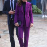 Kate Middleton ve fialovém kalhotovém kostýmku, který zkombinovala s černými lodičkami, černým prošívaným psaníčkem a kruhovými náušnicemi.

Pokud byste si na českých e-shopech chtěla pořídit podobný outfit, jeho celková cena by činila zhruba 16 241 Kč.