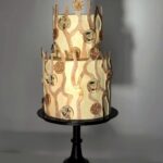 Dvoupatrový dort v bílo-zlatavých odstínech má uvnitř hned několik dalších vrstev.