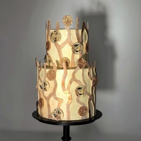 Dvoupatrový dort v bílo-zlatavých odstínech má uvnitř hned několik dalších vrstev.