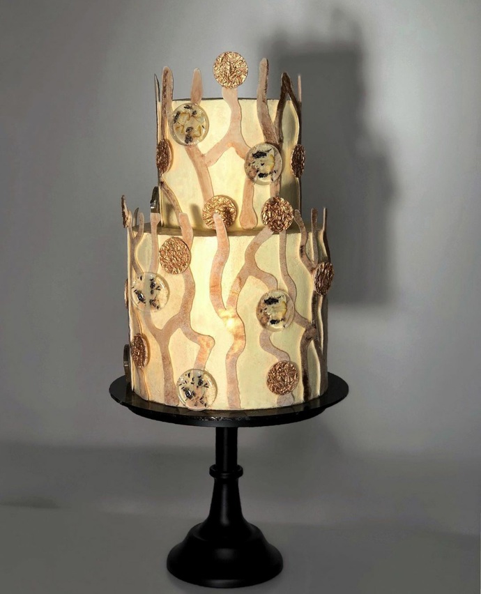 Dvoupatrový dort v bílo-zlatavých odstínech má uvnitř hned několik dalších vrstev.