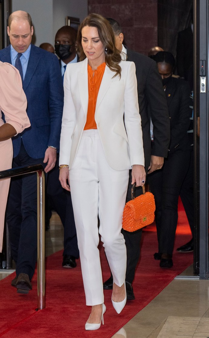 Kate Middleton v elegantním bílém kalhotovém kostýmku, který zkombinovala s oranžovou halenkou a bílými lodičkami do špičky. Na českých e-shopech byste za podobný outfit utratila okolo 4606 Kč.