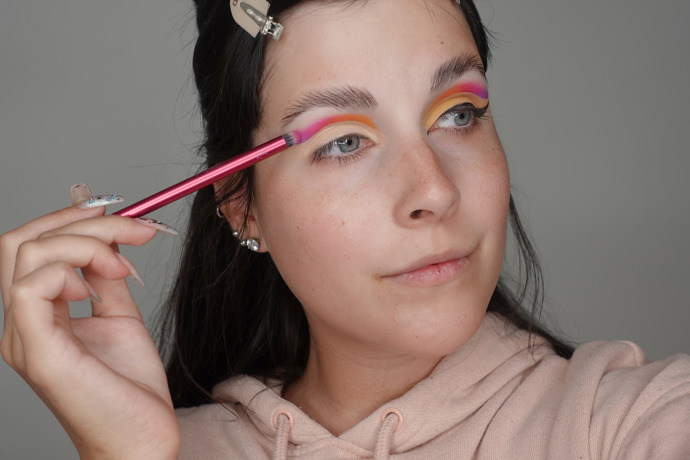 Na víčko naneste bázi pod oční stíny a následně začněte vedle sebe vrstvit barevné stíny od vnitřního koutku po vnější. Vždy je částečně překryjte přes sebe, aby vznikl hezký barevný přechod.