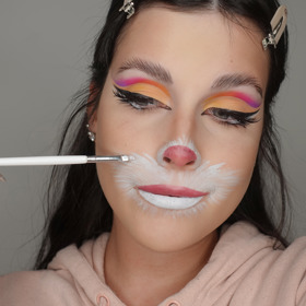 Po dolíčení očí, nanesení umělých řas a make-upu nakreslete bílou vodovou barvou kolem pusy a nosu náznak králičích chlupů. Na nos a rty nakreslete růžovou tekutou rtěnkou čumáček, abyste podpořila iluzi velikonočního zajíčka.