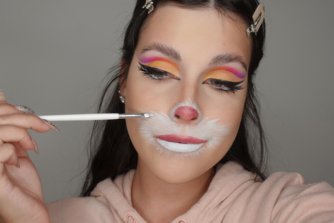 Po dolíčení očí, nanesení umělých řas a make-upu nakreslete bílou vodovou barvou kolem pusy a nosu náznak králičích chlupů. Na nos a rty nakreslete růžovou tekutou rtěnkou čumáček, abyste podpořila iluzi velikonočního zajíčka.