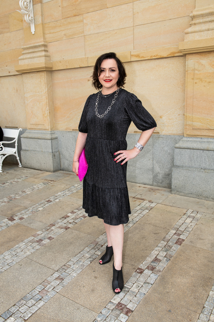 Šéfredaktorka Markéta Behinová oblékla stříbrno-černé blyštivé šaty Uterqüe, jež doplnila růžovým psaníčkem Bree, elegantními botami na vysokém podpatku s otevřenou špičkou a výraznými doplňky. 