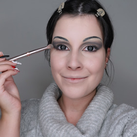 Pro stínování očí jsem použila především šedé a černé stíny, abych vytvořila dramatické líčení. Nebojte se stíny vytáhnout až k nově nakreslenému obočí. Korektorem jsem potom opticky zvětšila oční víčko pomocí techniky cut crease a nanesla na něj světlý perleťový stín. 