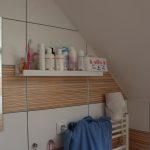 Druhá část kosmetiky, především holítka nebo šampony, se nacházejí na bílé poličce naproti oknu.