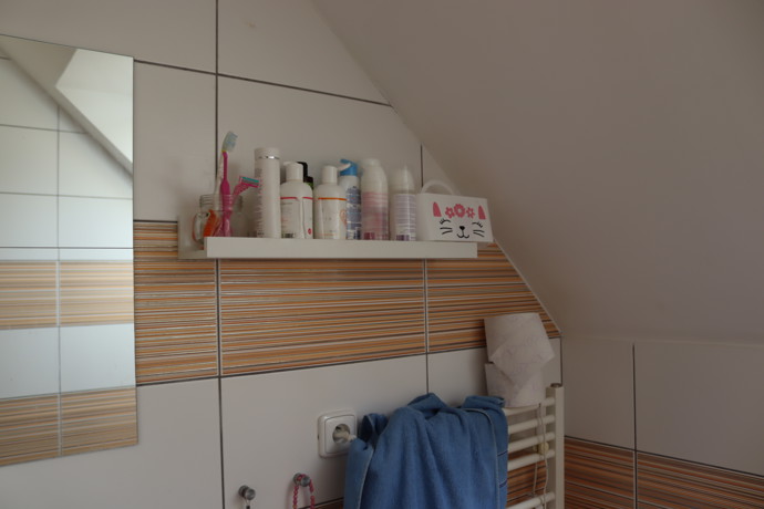 Druhá část kosmetiky, především holítka nebo šampony, se nacházejí na bílé poličce naproti oknu.