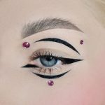 Asymetrický look vytvořený pomocí černých očních linek a různě velkých kamínků.