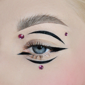 Asymetrický look vytvořený pomocí černých očních linek a různě velkých kamínků.