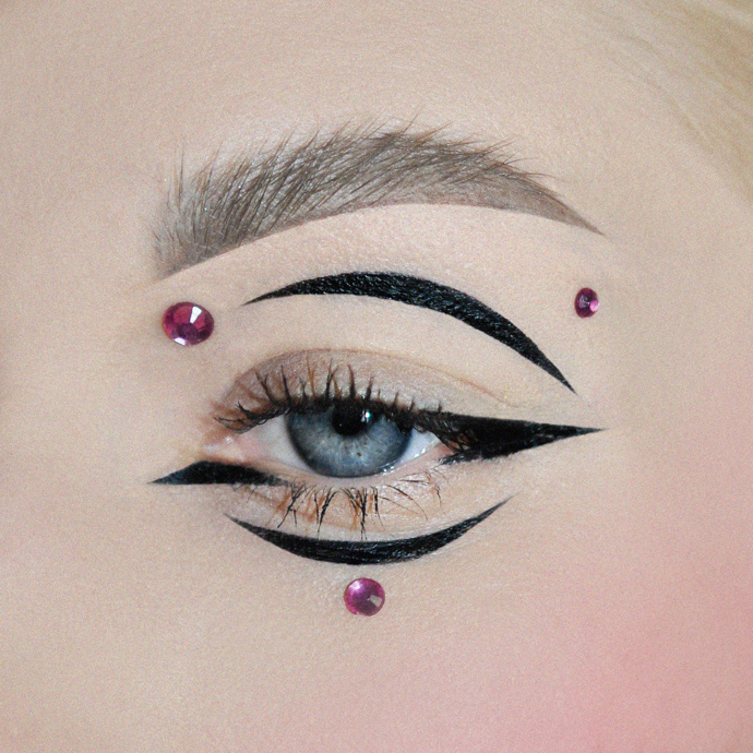 Asymetrický look vytvořený pomocí černých očních linek a různě velkých kamínků.
