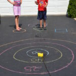 3. Namalujte křídami terč na zem a linii, od které se bude házet. Namísto šipek použijte houbičky na mytí nádobí či cokoliv jiného.