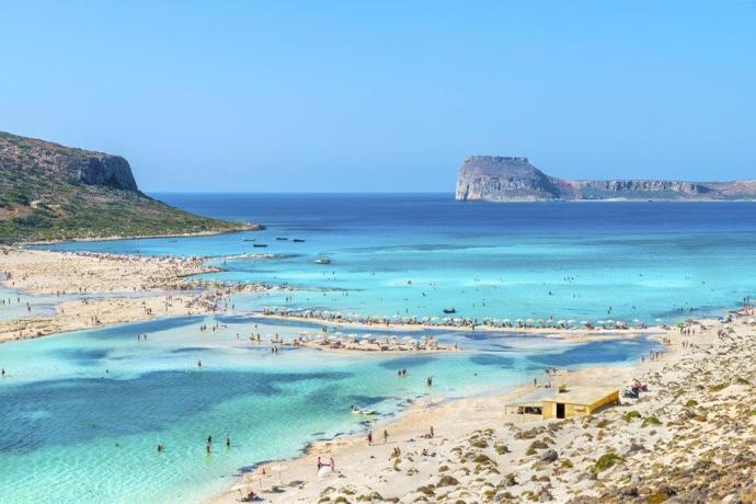 Balos, velká odměna za trochu námahy 

Na Balos se můžete vydat po vlastní ose pronajatým autem. Přibližně 8 km před příjezdem na parkoviště vás čeká závora, kde zaplatíte velmi symbolické vstupné 1 EUR za dospělou osobu, děti jsou zdarma. Věk dětí posuzují jen namátkovým nahlédnutím do auta. Poté vás čeká prašná, hrbolatá cesta, která se pozvolna vlní nahoru po srázu nad mořem a kterou je lepší zdolávat s velkou opatrností a maximální rychlostí 20 až 30 km/h. Přibližně po 6 km se dostanete na parkoviště (pokud je plné, zaparkujete za pomoci místního parkmistra podél silnice). Následně vás čeká ještě dvoukilometrový, nejdříve mírný a později příkřejší, sestup k pláži. Po cestě dolů i nahoru se vám naskytnou krásné výhledy, člověk má stále tendenci zastavovat a fotit a fotit a fotit. Na pláži jdou pronajmout plážové sety za 7 nebo 8 EUR a je tu i stánek s občerstvením.   Vzhledem k tomu, že přístup k pláži není bez námahy, je na Balosu o poznání méně lidí než na Elafonisi. Ačkoli někoho může Elafonisi okouzlit více, díky čisťounké vodě a jemnému písku bez nástrah oceníte také Balos.
