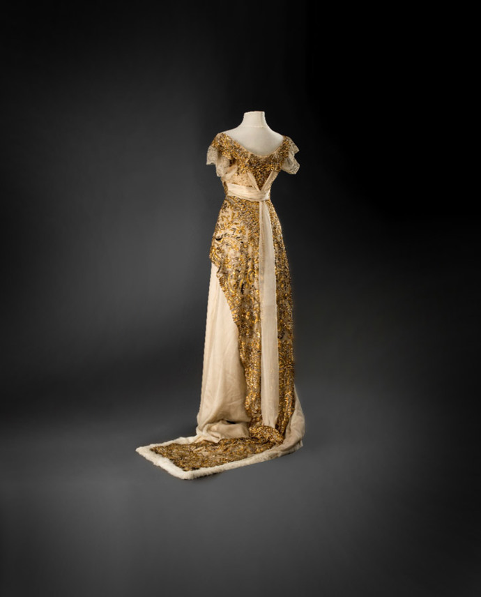 Plesová toaleta s tunikou, 1912–1913, vídeňský salon L.&H. Laufer, hedvábný satén a šifon, strojová krajka, výšivka lamelami a korálky, kožešinový lem (ze sbírek Uměleckoprůmyslového musea v Praze) Plesová toaleta s tunikou, 1912–1913, vídeňský salon L.&H. Laufer, hedvábný satén a šifon, strojová krajka, výšivka lamelami a korálky, kožešinový lem (ze sbírek Uměleckoprůmyslového musea v Praze)