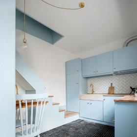Kdyby schody končily až na zemi, už by překážely u kuchyňské linky, a tak architekti přidali malou podestu, která pomáhá výškový rozdíl překonat a zároveň slouží jako lavice s úložným prostorem.
