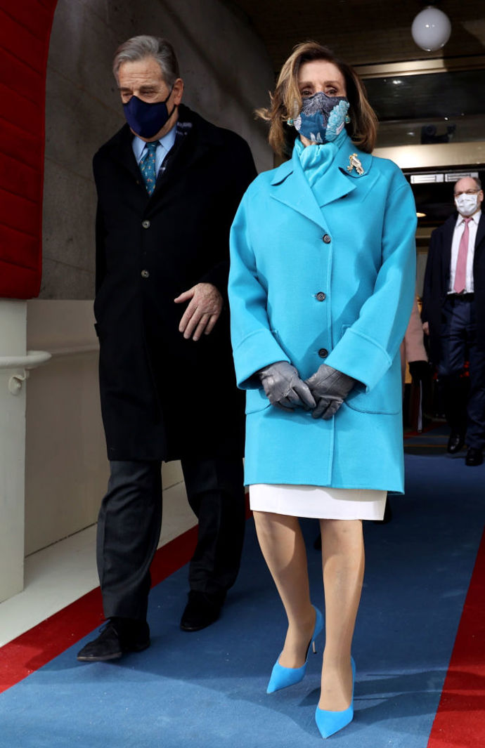 Nancy Pelosi, mluvčí House of Representatives, oblékla zářivě modrý kabát se sladěnými lodičkami, šálou a vzorovanou rouškou.
