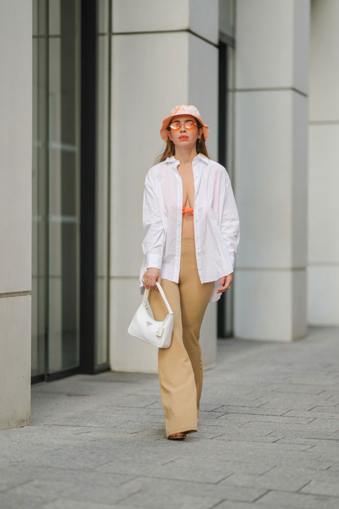 Výrazný bucket hat v oranžové barvě vypadá skvěle k bílé košili a béžovým kalhotům.
