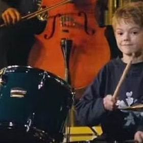 Thomas Brodie-Sangster hrající na bicí ve snímku Láska nebeská
