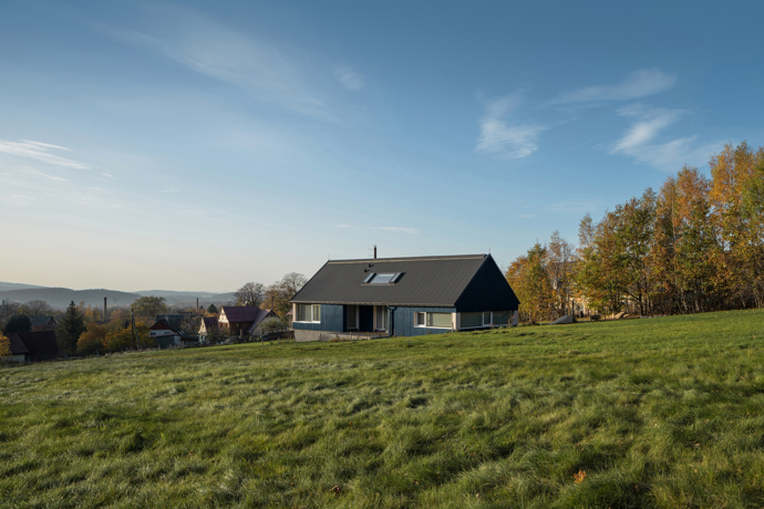 Modrý šindelový obklad a elegantní bílé rámy oken vytvářejí kontrast, který nemůžete přehlédnout. Architektka Markéta Cajthamlová a její tým se postarali o každý detail, ať už jde o interiér plný dřeva nebo promyšlenou dispozici, která nabídne vše, co potřebujete.
