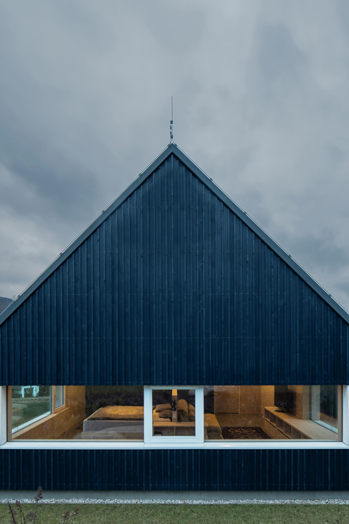 Modrý šindelový obklad a elegantní bílé rámy oken vytvářejí kontrast, který nemůžete přehlédnout. Architektka Markéta Cajthamlová a její tým se postarali o každý detail, ať už jde o interiér plný dřeva nebo promyšlenou dispozici, která nabídne vše, co potřebujete.
