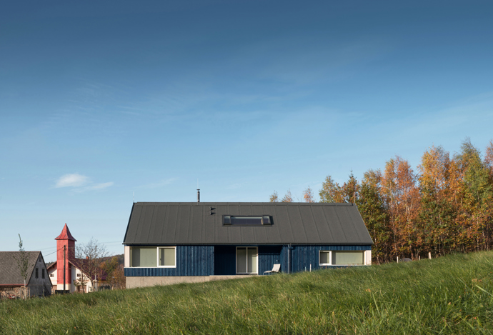Modrý šindelový obklad a elegantní bílé rámy oken vytvářejí kontrast, který nemůžete přehlédnout. Architektka Markéta Cajthamlová a její tým se postarali o každý detail, ať už jde o interiér plný dřeva nebo promyšlenou dispozici, která nabídne vše, co potřebujete.
