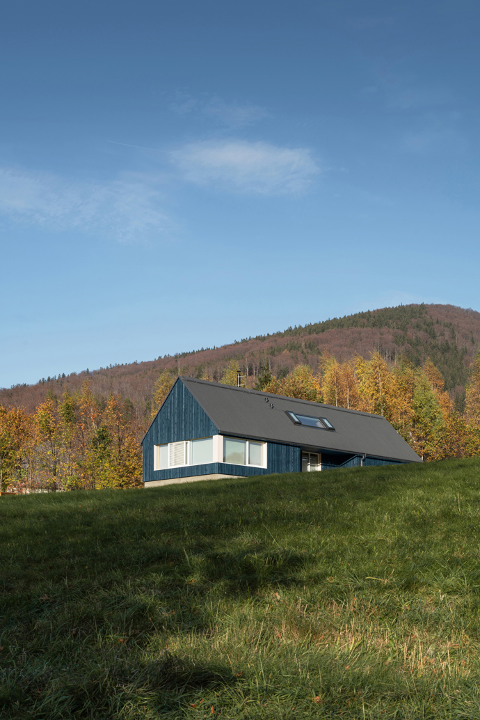 Modrý šindelový obklad a elegantní bílé rámy oken vytvářejí kontrast, který nemůžete přehlédnout. Architektka Markéta Cajthamlová a její tým se postarali o každý detail, ať už jde o interiér plný dřeva nebo promyšlenou dispozici, která nabídne vše, co potřebujete.
