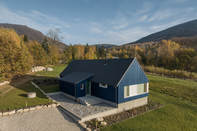 Modrý šindelový obklad a elegantní bílé rámy oken vytvářejí kontrast, který nemůžete přehlédnout. Architektka Markéta Cajthamlová a její tým se postarali o každý detail, ať už jde o interiér plný dřeva nebo promyšlenou dispozici, která nabídne vše, co potřebujete.
