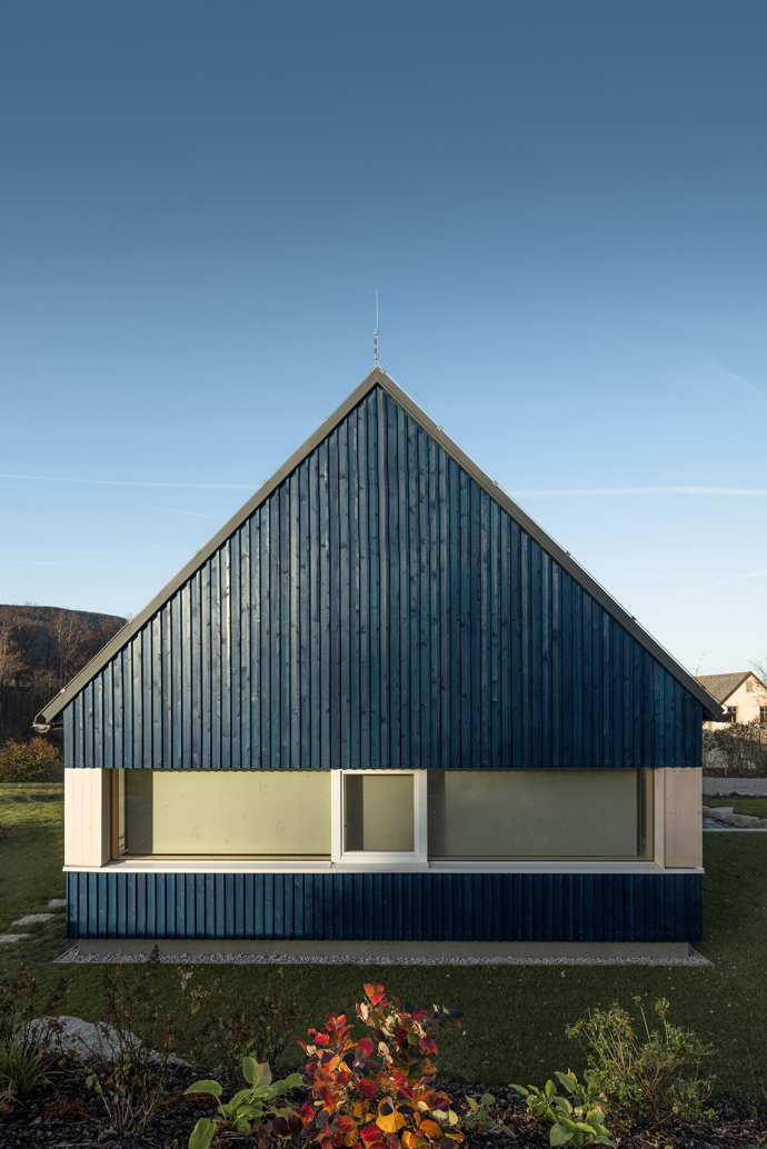 Modrý šindelový obklad a elegantní bílé rámy oken vytvářejí kontrast, který nemůžete přehlédnout. Architektka Markéta Cajthamlová a její tým se postarali o každý detail, ať už jde o interiér plný dřeva nebo promyšlenou dispozici, která nabídne vše, co potřebujete.
