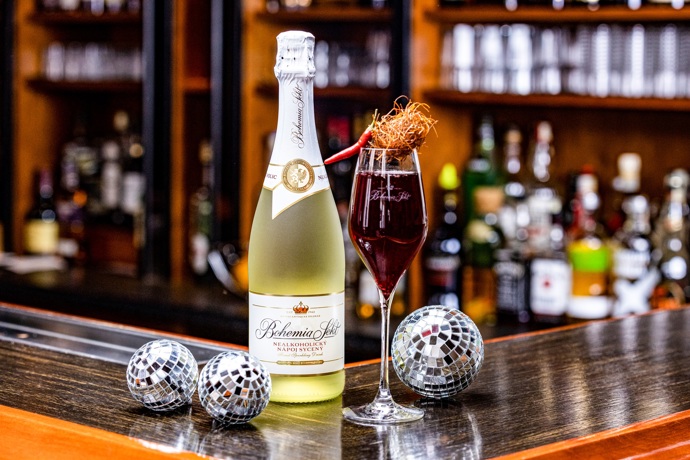Stejné zadání jako AI obdržel i profesionální barman Martin Vogeltanz. Nechte se inspirovat jeho recepturou.

Hot Bubbles

ingredience: 10 cl nealkoholického Bohemia Sektu, 10 cl ibiškového cordialu (ibišek, cukr, voda, chilli papričky), 0,5 cl čokoládového sirupu

na ozdobu: chilli paprička, chilli nitky

Do vychlazené sklenice odměřte ibiškový cordial, čokoládový sirup a dolijte Bohemia Sektem. Lehce lžičkou promíchejte a ozdobte chilli papričkou a chilli nitkami. Pro nejlepší možnou chuť drinku mějte všechny ingredience dobře vychlazené. 

Příprava ibiškového cordialu: Připravte silný ibiškový výluh z 0,5 litru vody a 15 g ibiškového čaje. Do teplého čaje přidejte 90 g cukru a chilli papričku podle chuti.
