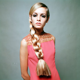Twiggy pózuje v šik růžových mini šatech. Její ikonický účes "na kluka" stylisté pro toto focení obměnili použitím umělého silného copu. 
