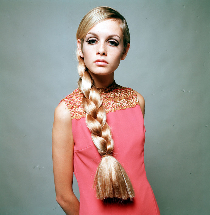 Twiggy pózuje v šik růžových mini šatech. Její ikonický účes "na kluka" stylisté pro toto focení obměnili použitím umělého silného copu. 
