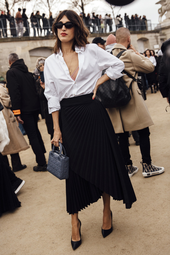 Jeanne Damas oblékla na přehlídku Dior nadčasovou kombinaci bílé košile a černé plisované sukně, outfit doplnila malou kabelkou Lady Dior.

