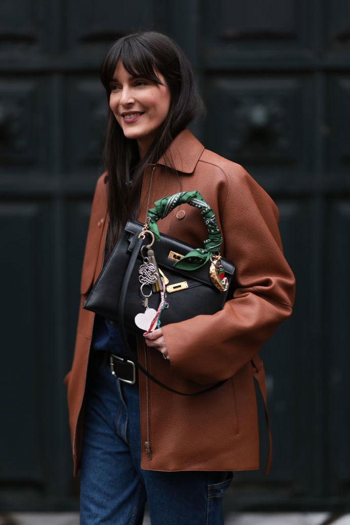 Klasická černá kabelka od Hermès samozřejmě nikdy nemůže vypadat nudně, ale pokud byste jí chtěla dodat na osobitosti, omotejte kolem ucha barevný hedvábný šátek a přidejte pár přívěsků.
