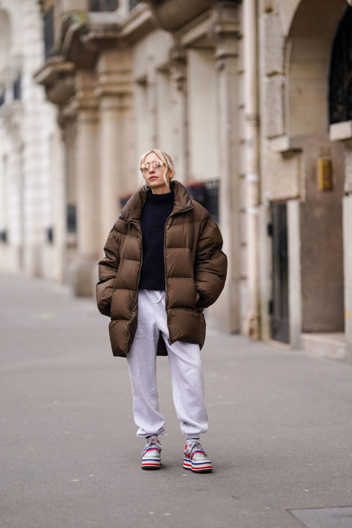 Šedé tepláky, tmavě modrý svetr, hnědá péřová puffer bunda a tenisky na platformě – pohodlný víkendový outfit je na světě!
