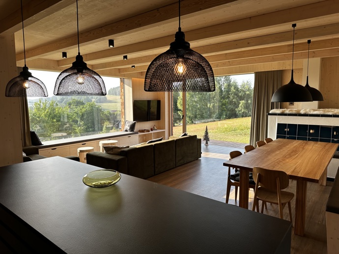 Přírodní minimalistický design a decentní barevná paleta zajišťuje dokonalou eleganci. Velkými okny proudí dovnitř mnoho světla, přes které je možné pozorovat malebnou krajinu, která celou chatu obklopuje. Fasádu domu tvoří ručně štípané modřínový šindel, zatímco uvnitř je obloženo smrkovými biodeskami.
